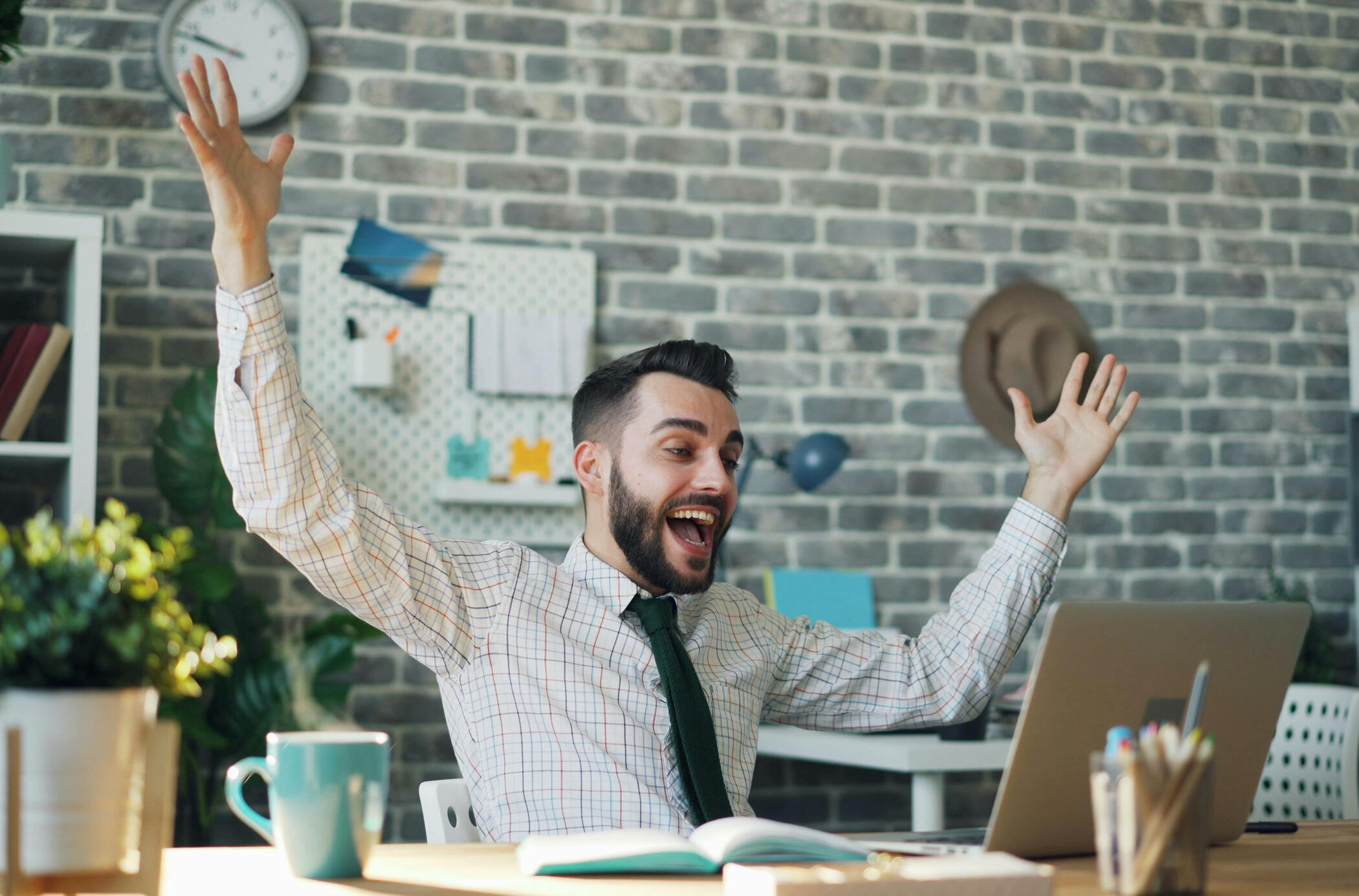 Excited business owner celebrating on laptop at desk, illustrating the Merchant Rewards Cash Discount Processing